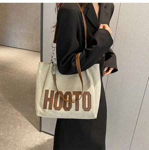 Détail du sac cabas en toile crème avec lettrage marron et bandoulière à chaîne élégante