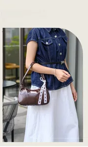 Brown leather underarm bag with white lace ribbon detail in a street style setting