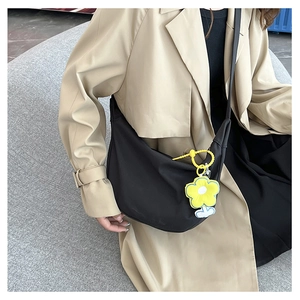 Détail du sac croissant noir en toile avec breloque fleur jaune et bandoulière large