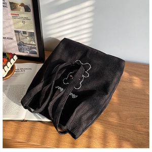 Dettaglio borsa tote in velluto a coste nero con ricamo a forma di orso su tavolo di legno