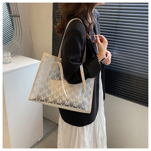 Detail of transparent PVC tote bag with white M-letter pattern and beige leather trim