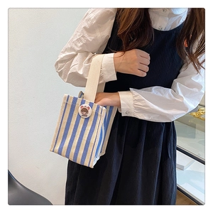 Detailed shot of striped canvas handbag with cute cartoon badge and sturdy white handles