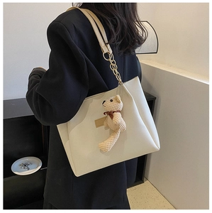 Detail of cream PU tote bag featuring gold chain strap and cute knit bear charm
