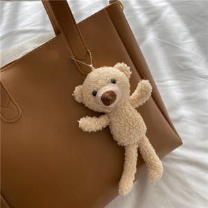 Cute teddy bear plush charm in beige sherpa fleece hanging on a leather tote bag