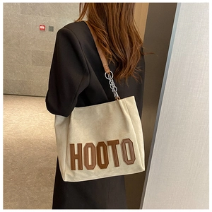 Détail du sac cabas crème avec lettrage HOOTO marron et détails de bandoulière en chaîne argent