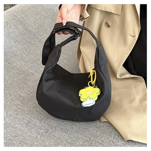 Détail du sac demi-lune en nylon noir avec breloque fleur jaune et bandoulière large