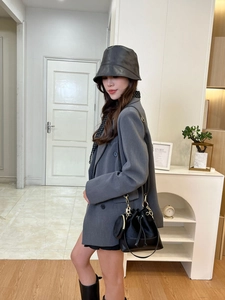 Fashionable black drawstring bucket bag with gold chain strap on a stylish gray blazer