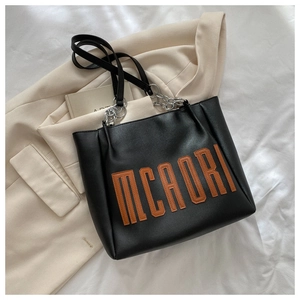 Détail du sac cabas en PU noir avec patch lettre orange et bandoulière chaîne argent