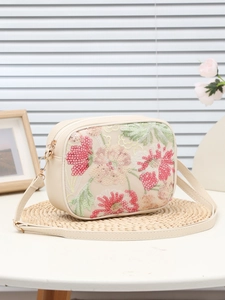 Dettaglio dei ricami floreali di paillettes rosa su borsa a tracolla color crema