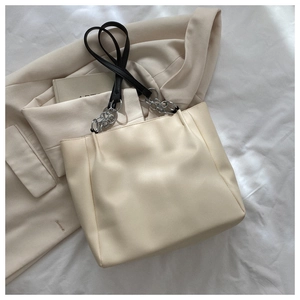 Sac cabas beige avec bandoulière noire et chaîne argentée sur un fond artistique