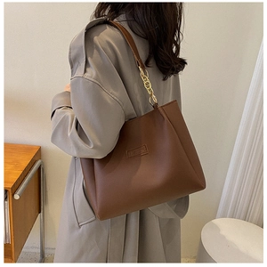 Detail of a brown leather tote bag showing a metal chain strap and the fashion logo label