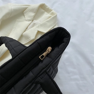 Minimalist black quilted puffer tote bag with elegant golden zipper closure