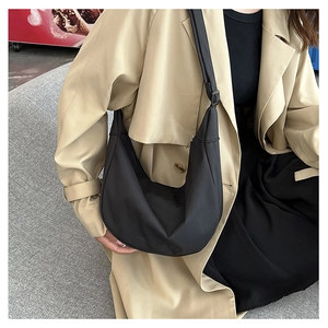 Détail d'un sac bandoulière noir en forme de croissant avec sangle large sur un mannequin