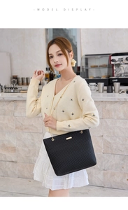 Detail of a black quilted tote bag with gold chain strap worn by a model in a cafe