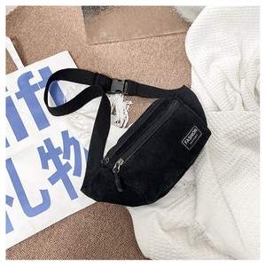 Detail of black corduroy waist bag with a white woven label and adjustable woven strap