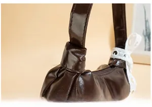 Detail of dark brown glossy shoulder bag with lace bow and knotted handle design