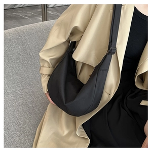 Vue détaillée d'un sac bandoulière noir en demi-lune porté avec un trench-coat beige chic