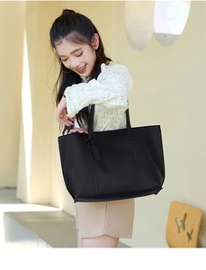Detail of a black matte faux leather tote bag with a minimalist shoulder strap and charm