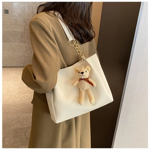 Close-up of white leather tote bag with a beige knitted bear charm and gold chain strap