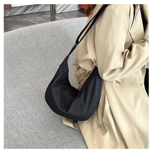 Détail d'un sac à bandoulière demi-lune noir assorti à un trench-coat classique élégant