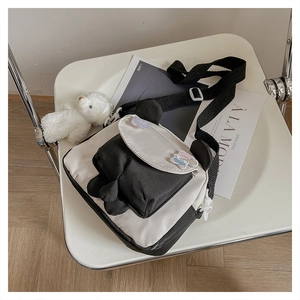 Detail of cute panda-style crossbody bag with bear pendant on a minimalist white chair