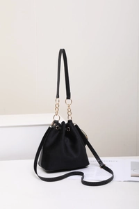 Detail of black suede drawstring bucket bag with gold chain and ring accents on white background