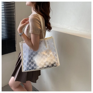 Close-up of clear PVC tote bag with white letter M pattern and cream PU leather handles
