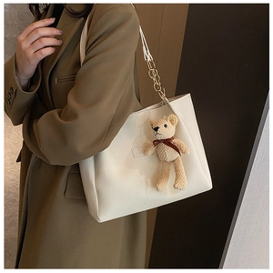 Detail view of cream tote bag with gold chain and a knit teddy bear charm accessory