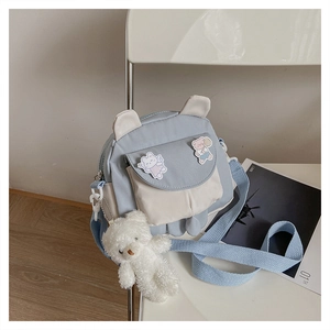 Detail of blue and white canvas crossbody bag with cartoon patches and plush bear charm