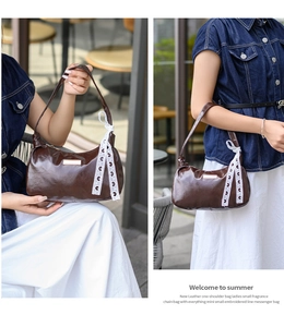 Detail of brown glossy leather shoulder bag featuring a white lace bow charm and metal plaque