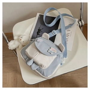 Detail of blue canvas bag featuring rabbit ears decoration and a plush bear pendant