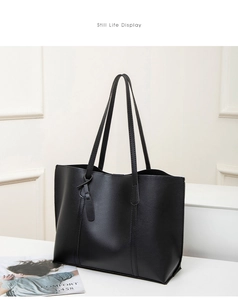 Detail view of large black tote bag with grain texture and decorative leather tag