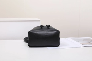 Detail view of black leather bucket bag with knotted handle accents on white surface