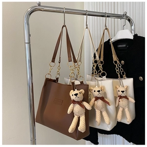 Detail view of large tote bags with FASHION embossing and teddy bear charms on metal rack