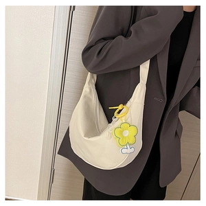 Gros plan du sac bandoulière blanc demi-lune avec breloque tournesol sur blazer foncé