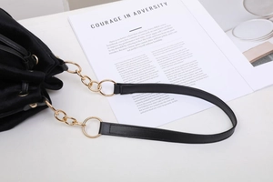 Detail of black velvet bucket bag showing gold hardware and leather strap on white surface
