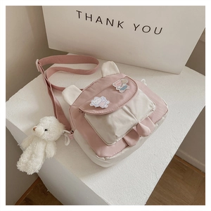 Detail of pink and white crossbody bag with cute bear ears, badges, and plush pendant