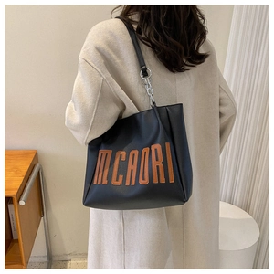 Détail du grand sac cabas noir avec patchs lettres et bandoulière chaîne sur un mannequin