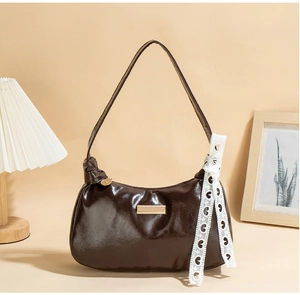 Detail of deep brown glossy PU leather underarm bag with gold metal plate and lace strap