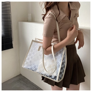 Detail of trendy semi-transparent tote bag with M-pattern and cream leather trim on model
