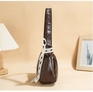 Detail of dark brown glossy underarm bag featuring a delicate white lace bow decoration