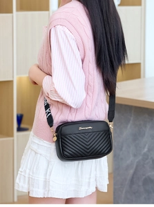 Detail of black camera bag featuring V-quilted pattern and a wide lettered nylon strap