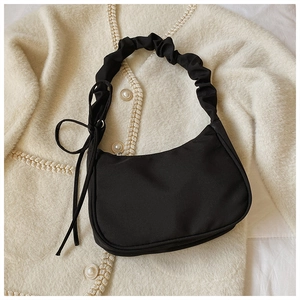 Detail einer schwarzen Hobo-Tasche mit Falten und Spitzenschleife auf Strickjacke