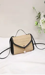 Detail of woven straw handbag with black leather trim, pearl charm, and gold buckle