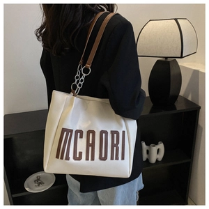 Détail du grand sac cabas crème avec lettres MCAORI et bandoulière porté par un mannequin