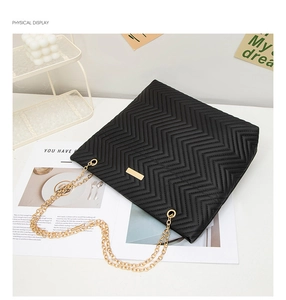 Detail of black quilted leather handbag with gold chain strap and textured V-stitch design