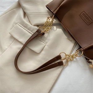 Classic dark brown PU leather tote bag with metal chain strap on beige blazer
