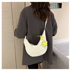 Détail d'un sac bandoulière demi-lune crème avec pendentif fleur jaune sur le côté