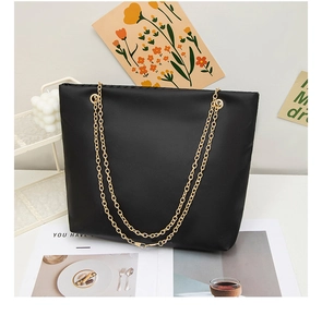 Detail view of black matte leather tote bag with elegant golden chain straps on white decor