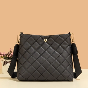 Sac seau matelassé noir avec boucle dorée et bandoulière en nylon sur fond chaleureux